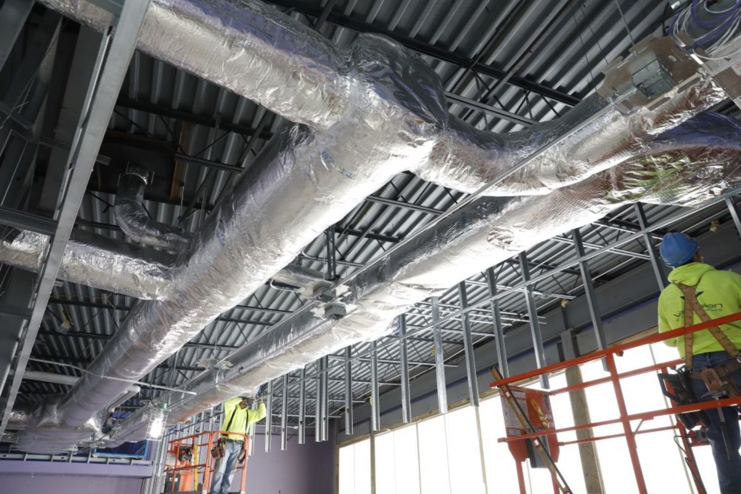 Workers installing ductwork in an office building, using tools and equipment to enhance the HVAC system.