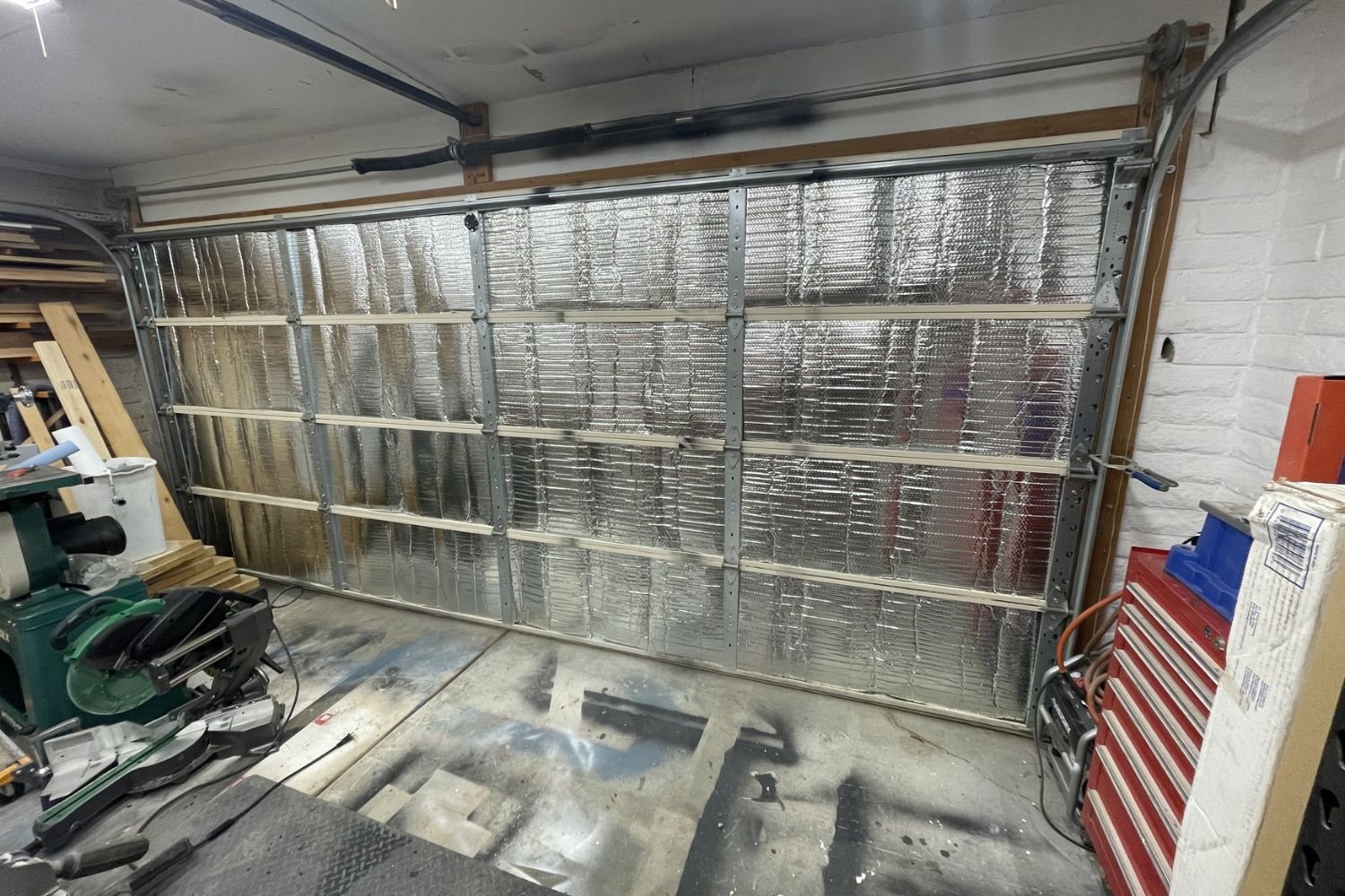 A partially insulated garage door with reflective foil, surrounded by tools and materials in a workshop setting.