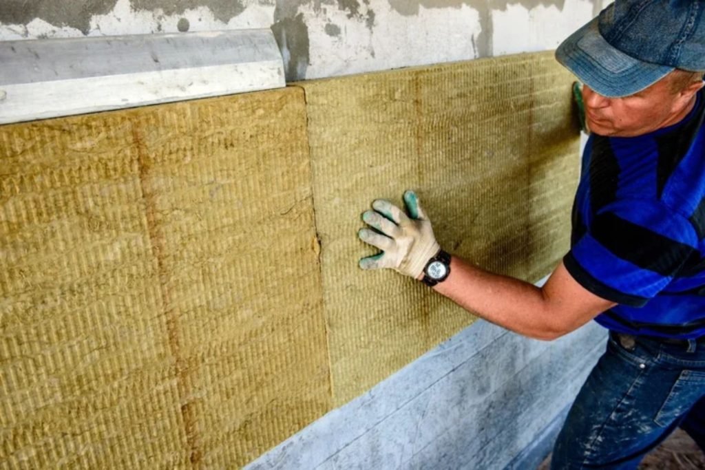 A man installs insulation on a wall, carefully placing the material to enhance energy efficiency in the space.