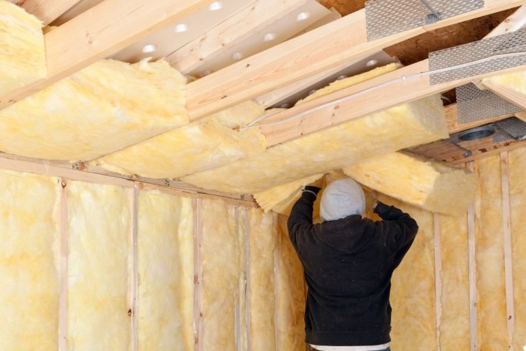A man installs insulation in a room, carefully placing material between the wall studs for energy efficiency.