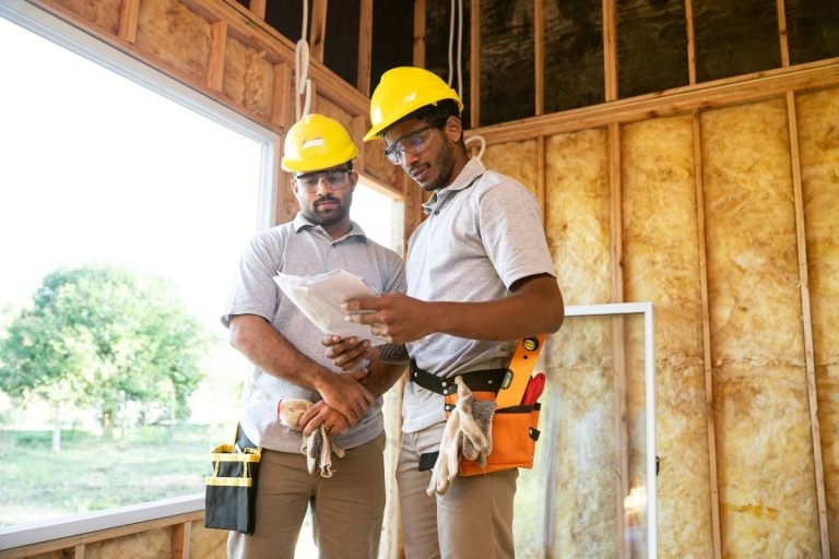 Two men in hard hats discussing plans at a construction site for an insulation project.
